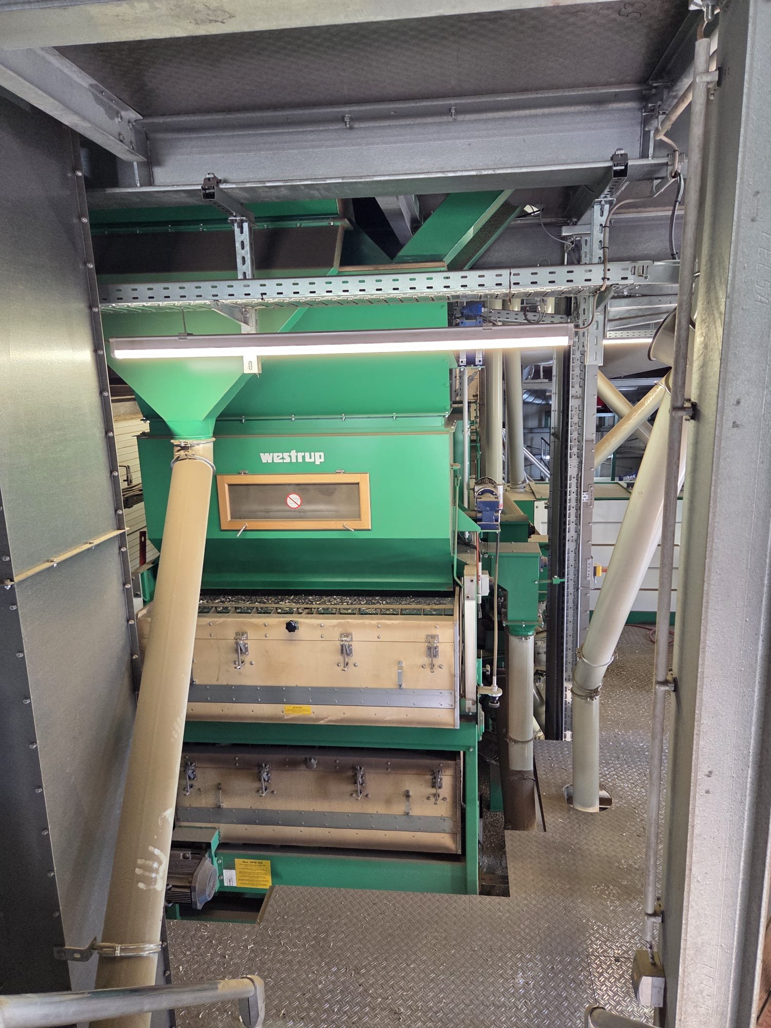 Industrial machinery with green components, pipes, and metal framework in a factory or plant setting.