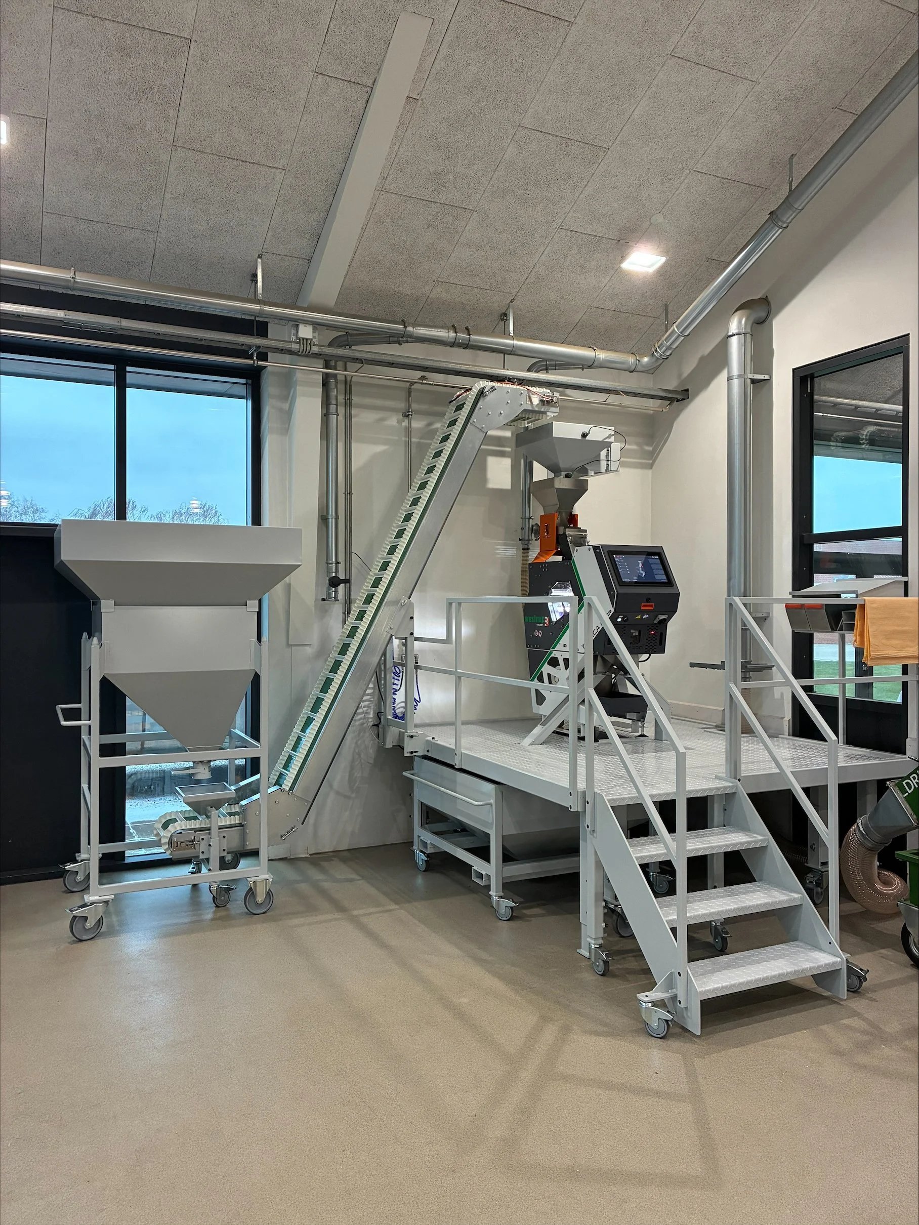 Industrial grain processing machine with a hopper, conveyor, and control panel in a modern facility.