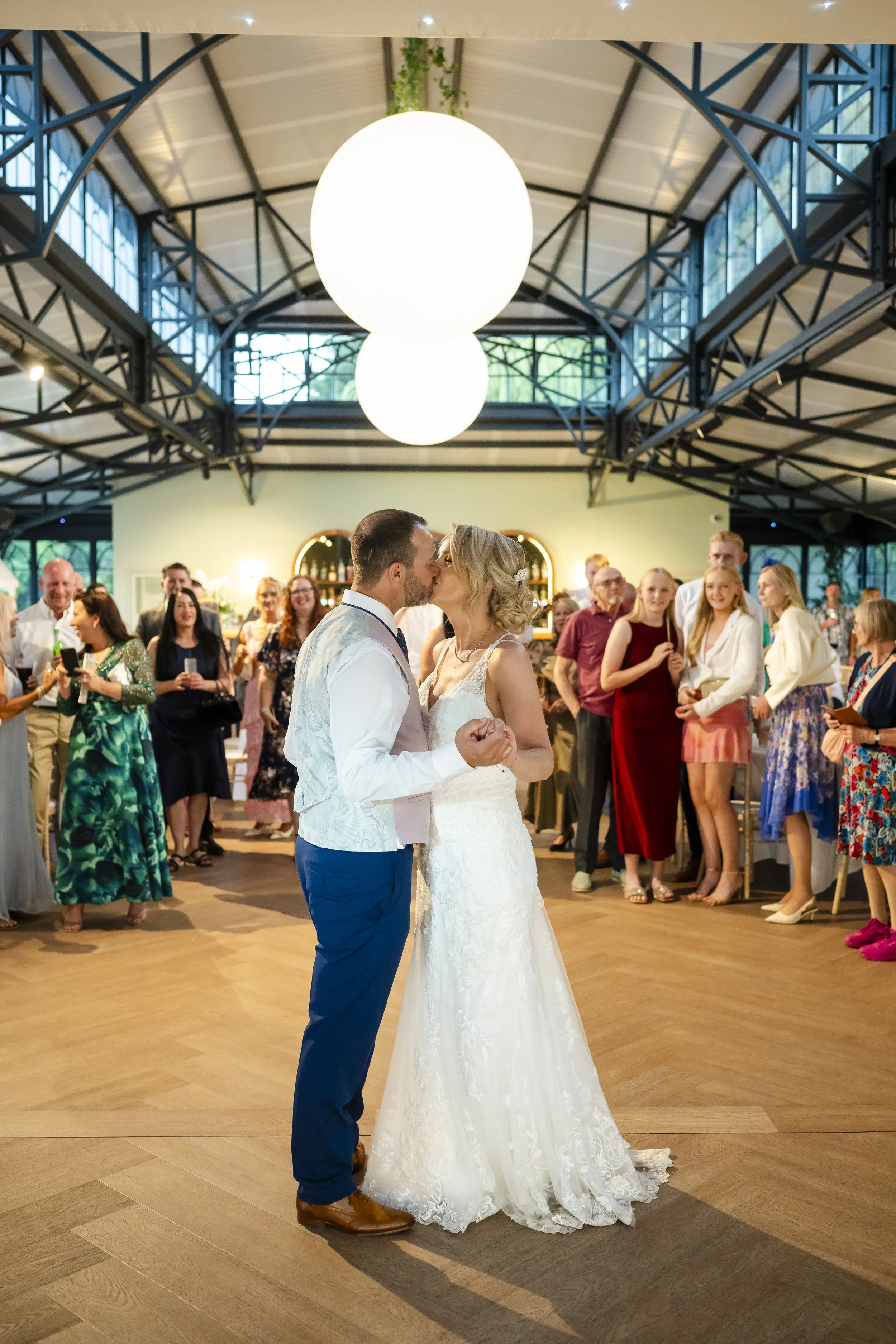 A bride and groom share their first dance at their wedding reception, surrounded by guests in a decorated indoor venue.
