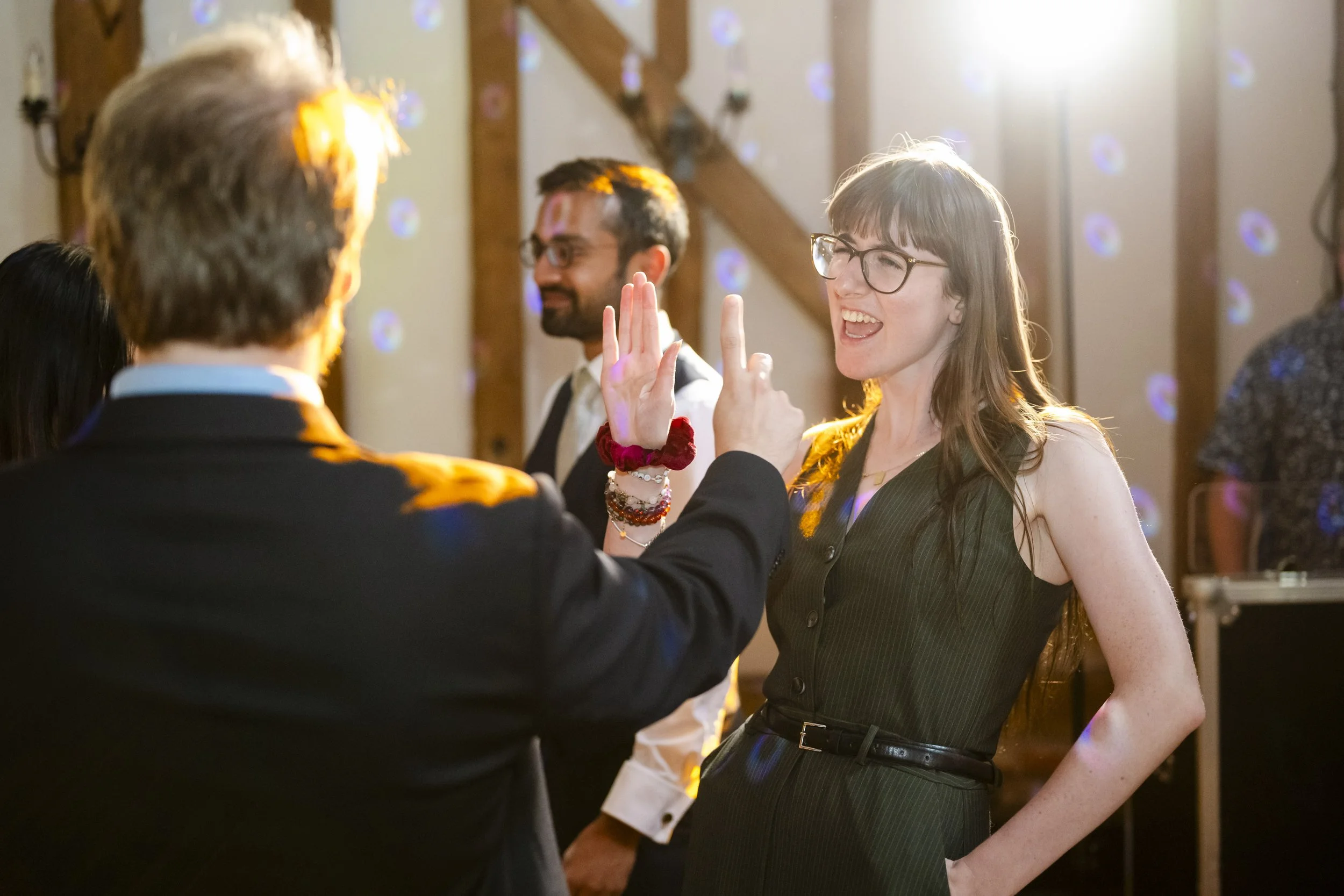 People dancing and socializing at a party or celebration in a decorated indoor venue with wooden beams and purple lights.