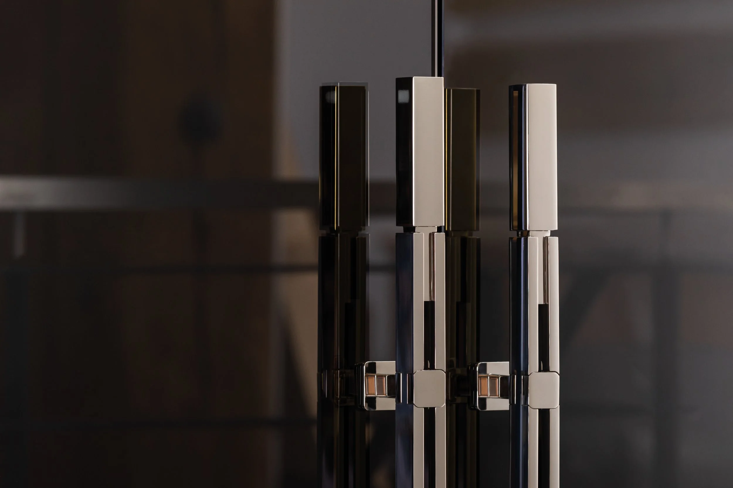 Close-up of a modern, abstract metallic sculpture with vertical rectangular and square bars reflecting light, set against a dark background.