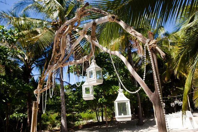 White lanterns and pearls hang from a wooden arch during a Costa Rica beach wedding in Santa Teresa