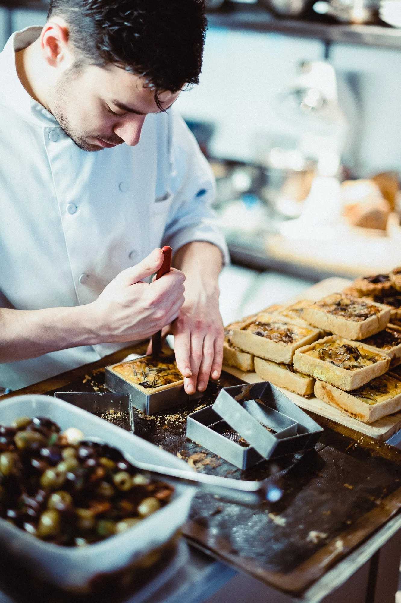 Chef cutting baked bread with toppings in a bakery kitchen.