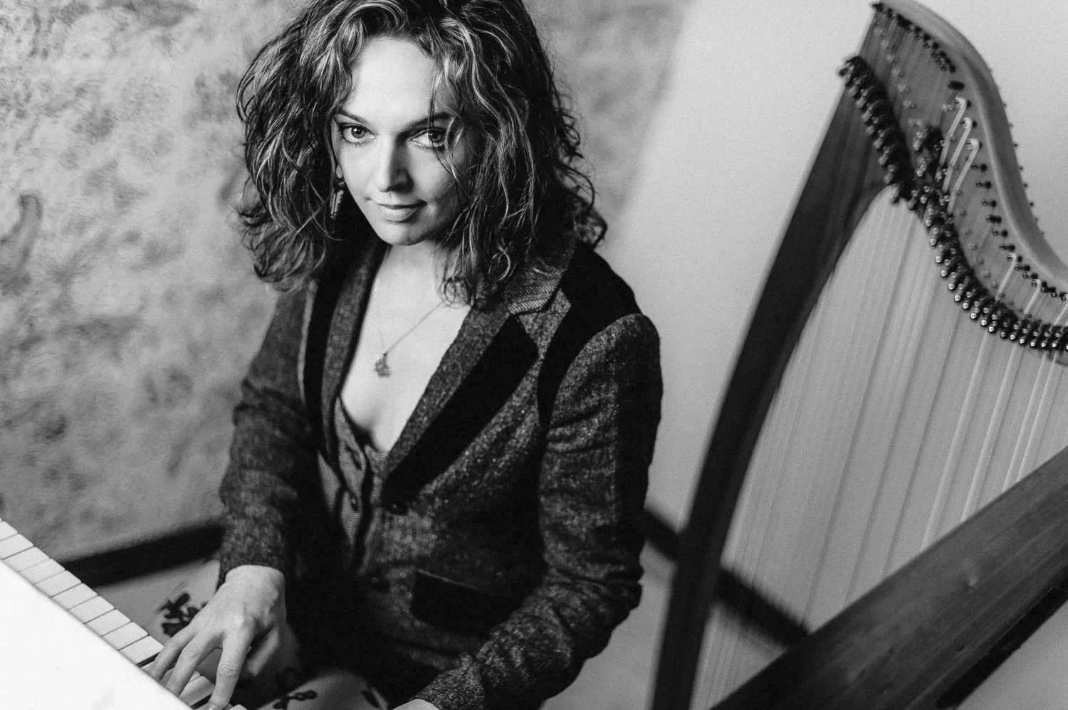 A woman with curly hair playing a piano, looking up at the camera, in a black and white photo.