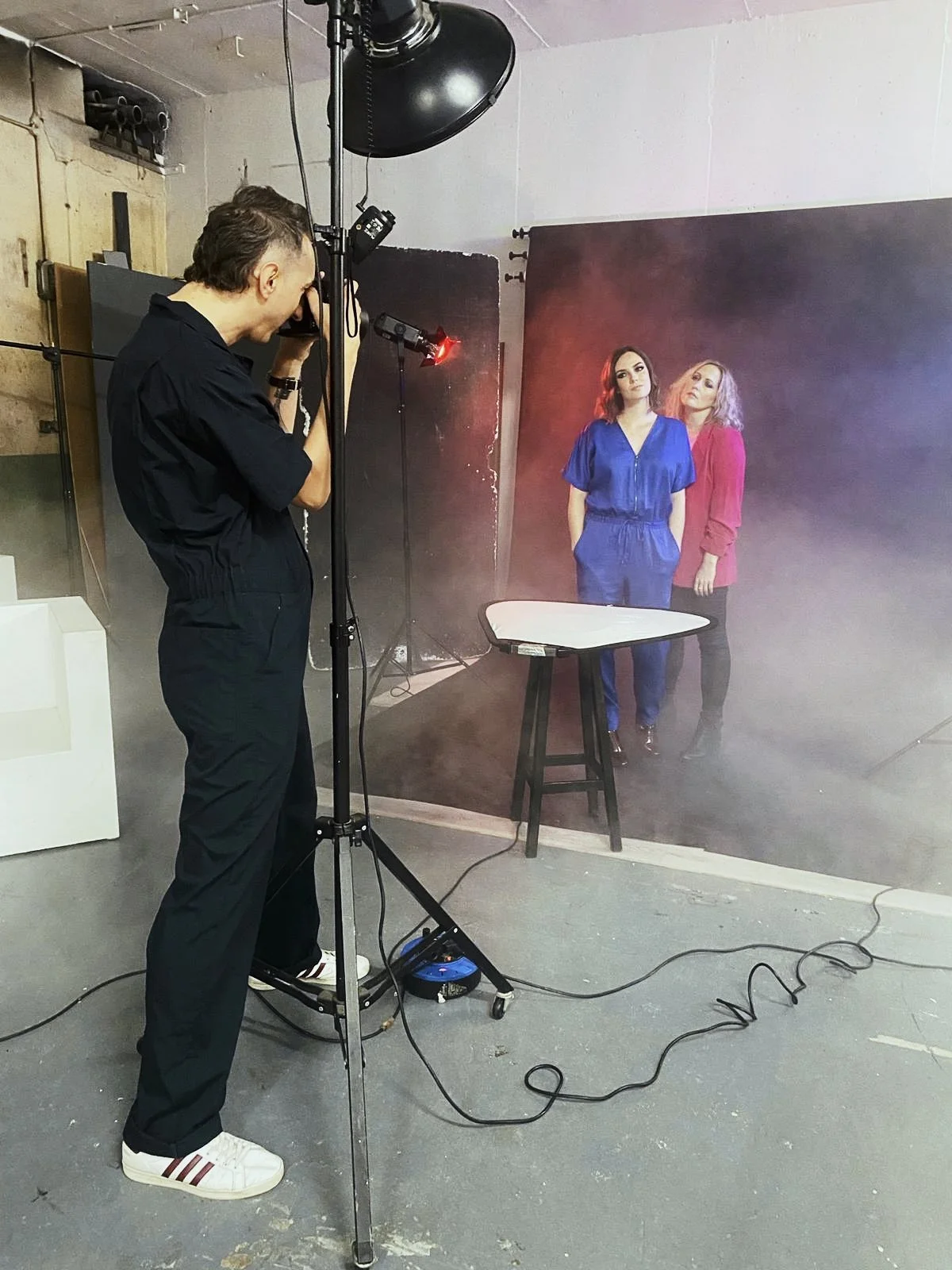 Photographer taking pictures of two women posing against a studio backdrop with fog and lighting effects.