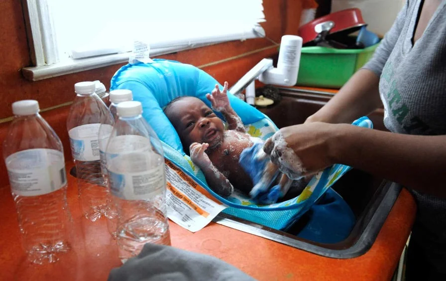 RACISM IN THE WATER: On January 28, 2016, Porshe Loyd uses bottled water to wash her three-week-old son, LeAndrew, in a baby bather in the kitchen sink at their home in Flint, Michigan.