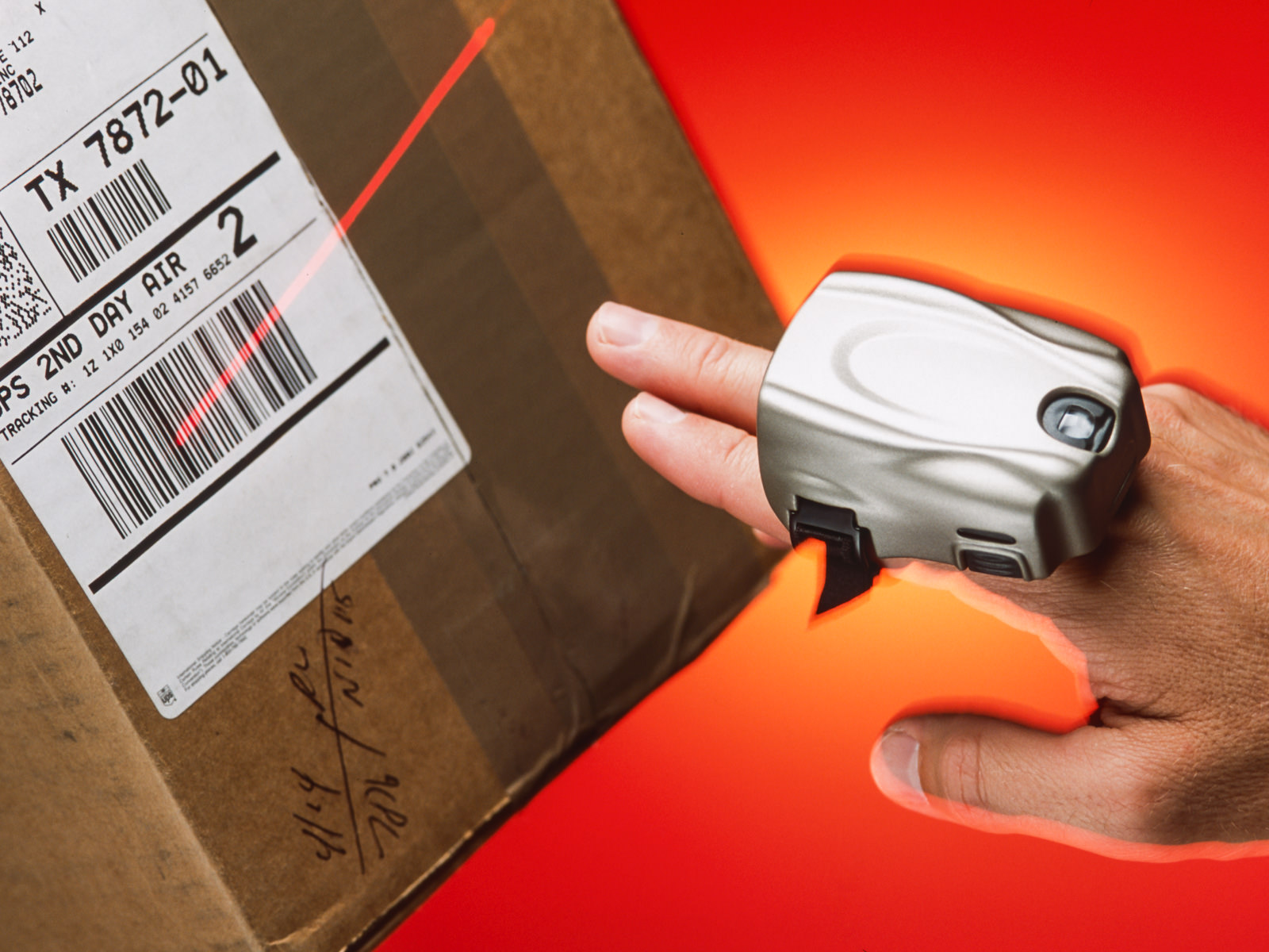 CRS1 ring scanner worn on the right first two fingers, pointed at a box and scanning a barcode