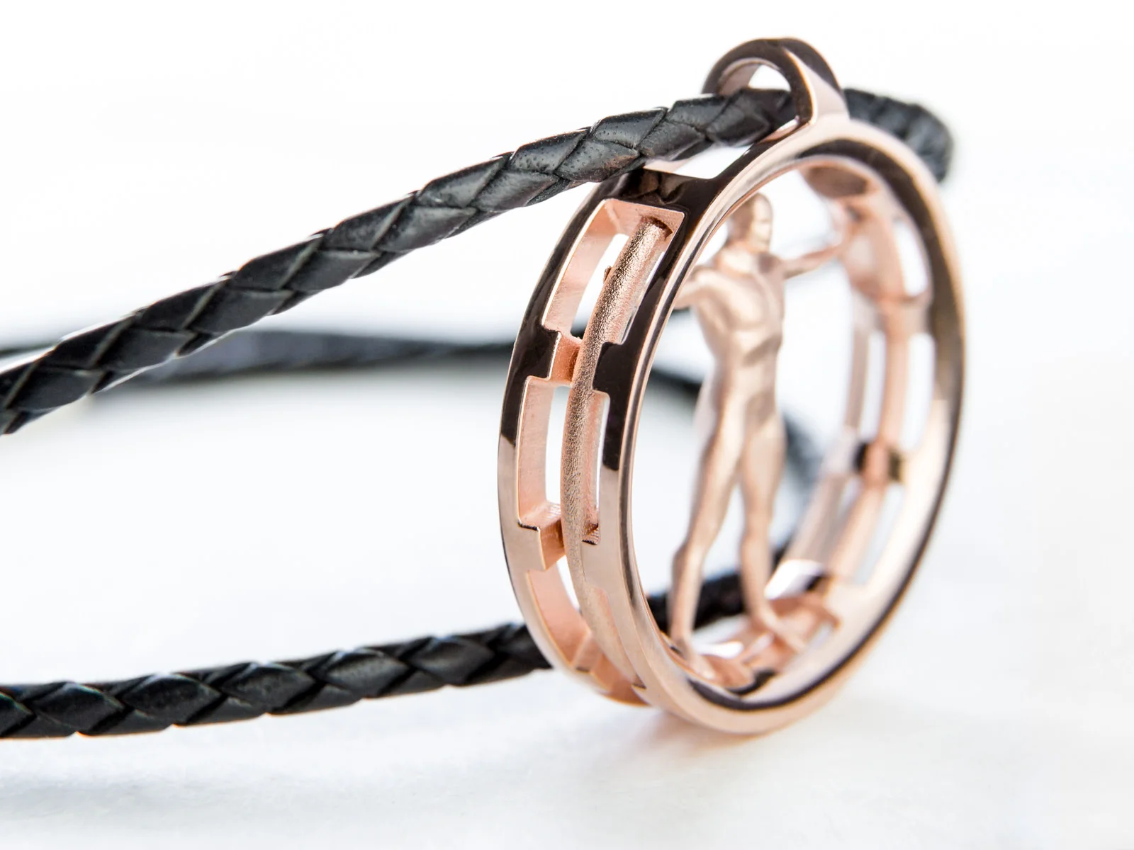 A rose gold Vitruvian man pendant with leather cord attached