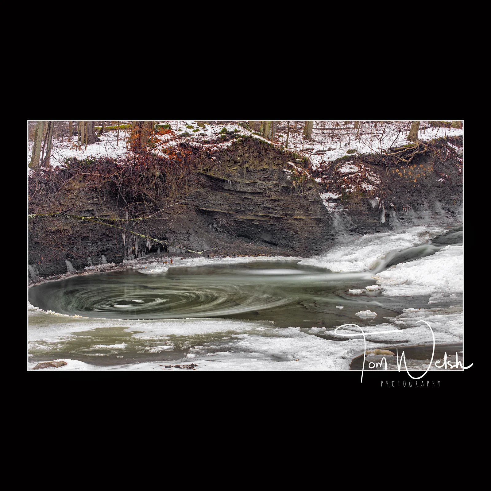 Water swirls as it tries to escape the frozen pool along the stream bed below the falls