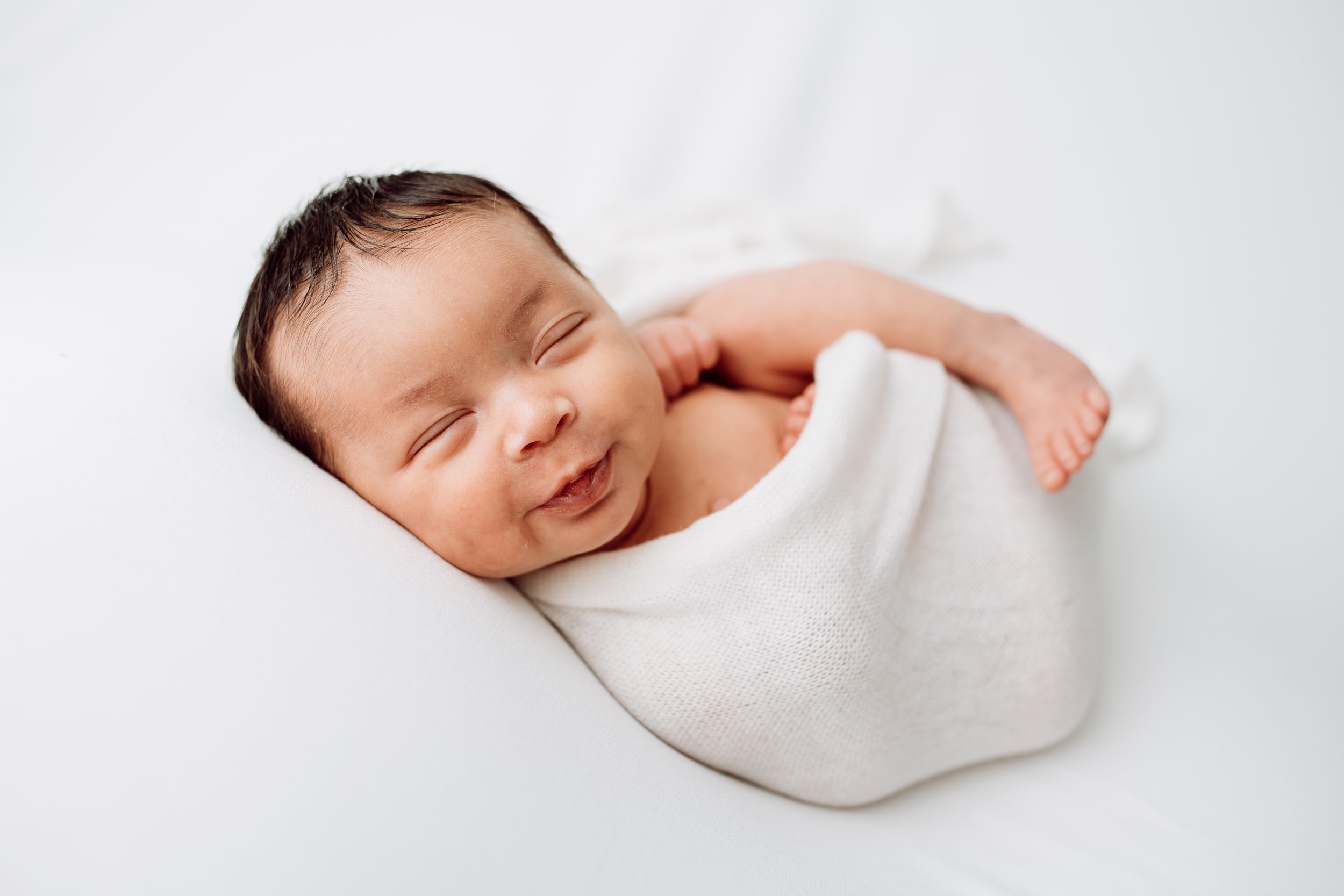 smiling newborn baby on all white fabric