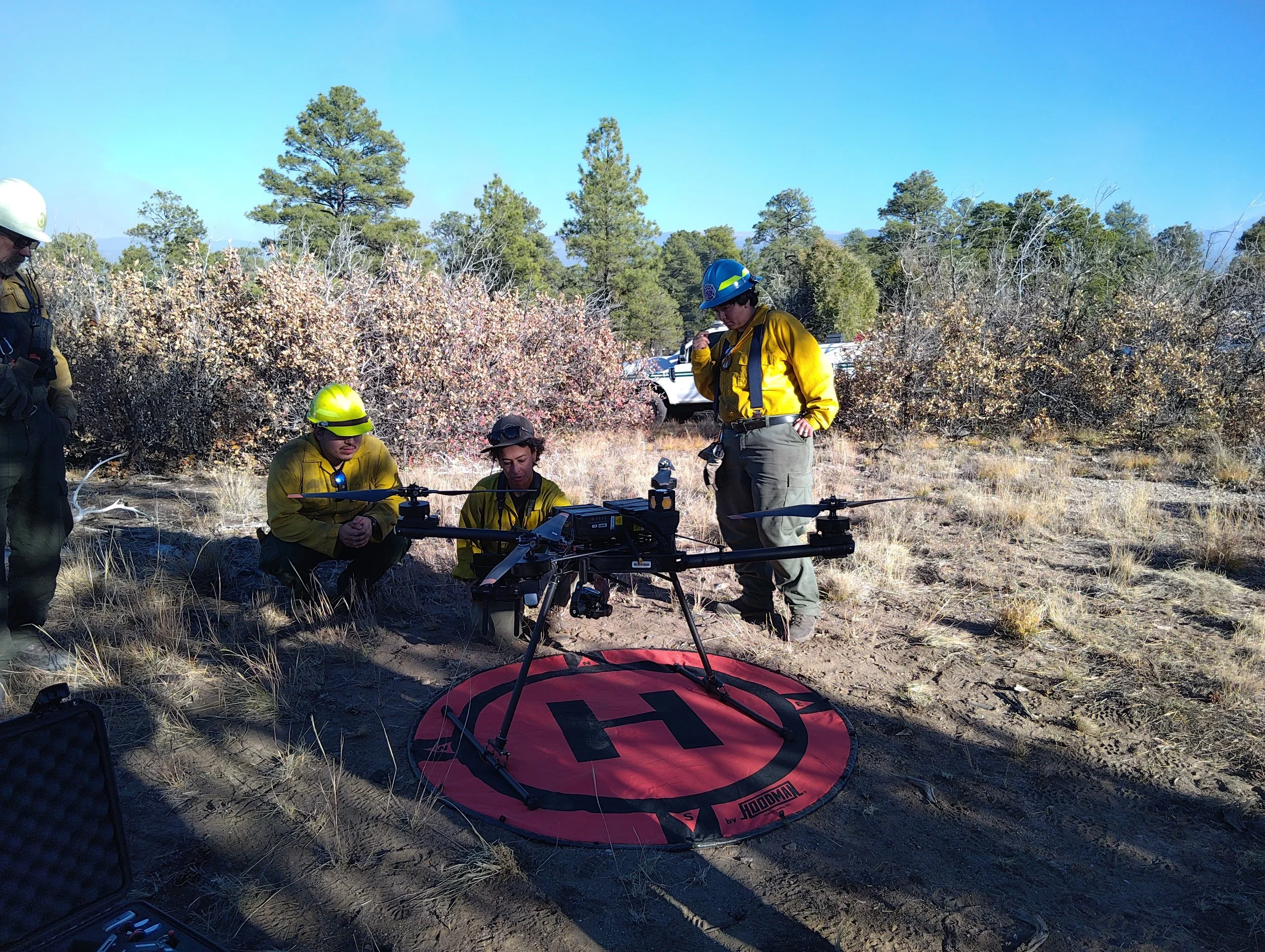 USFS UAS operator explains the system to members of the New Mexico’s All Hands All Lands Burn Team. Drone sits on a helipad landing.