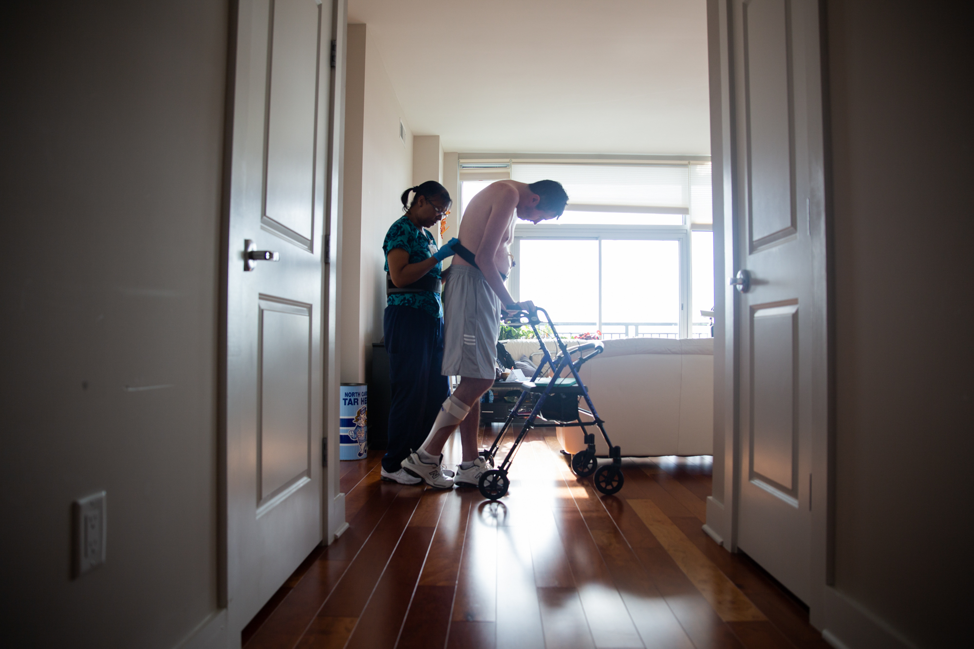  On Oct. 9, 2018, Lora Bradley helps Dr. Andrew Ross walk across his apartment in downtown Chapel Hill, NC. Dr. Ross was diagnosed with ALS in April 2017, and in August 2018 he decided that his ALS was bad enough that he needed around-the-clock care.