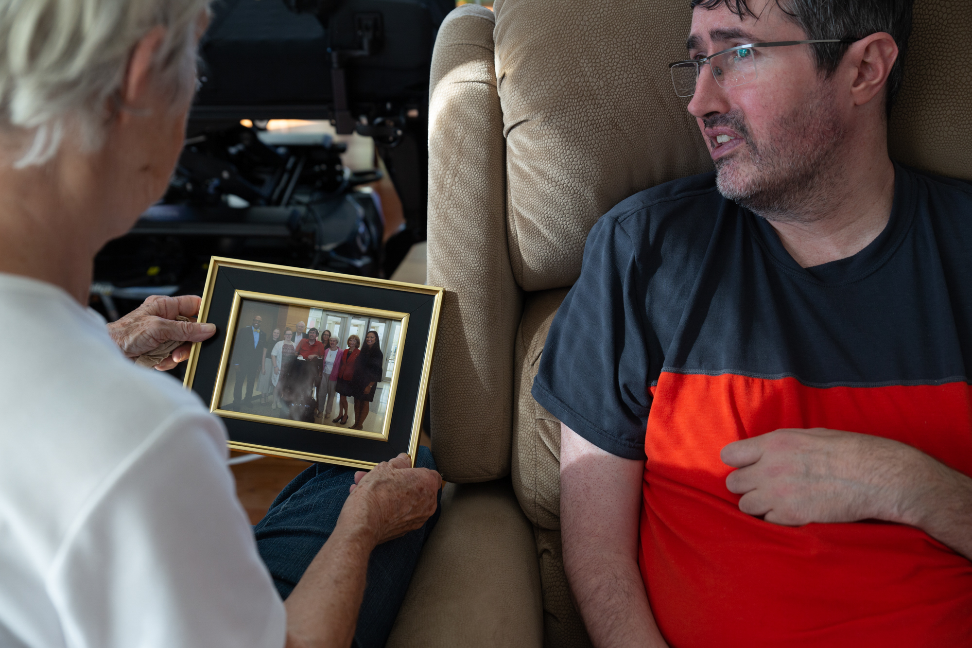  Andrew Ross talks to his mother, Mary, about her recent visit with Andrew’s father on Andrew’s behalf to Radford University. Andrew felt too sick that day so didn’t go. Mary Ross shows Andrew a past photo they all took at the university together, an