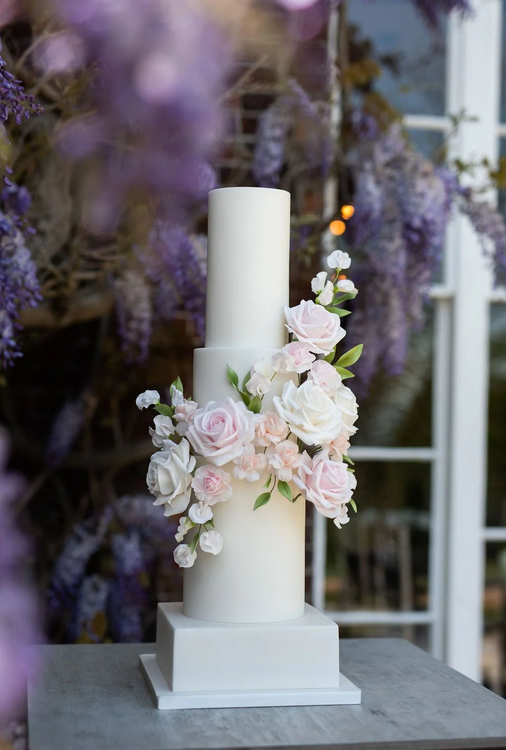 Modern white wedding cake with tall cylindrical tiers and handmade blush pink and ivory sugar flowers, created by a Surrey wedding cake maker.