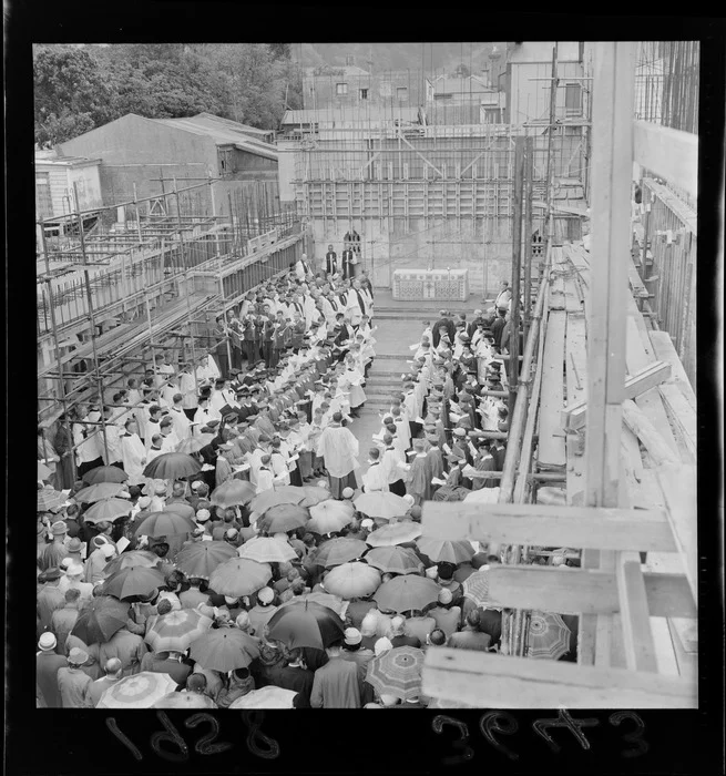Service in the roofless Anglican Cathedral, Wellington, under construction, with altar, choir and umbrellas. Evening post (Newspaper. 1865-2002) :Photographic negatives and prints of the Evening Post newspaper. Ref: EP/1958/3643-F. Alexander Turnbull Library, Wellington, New Zealand. /records/23259007