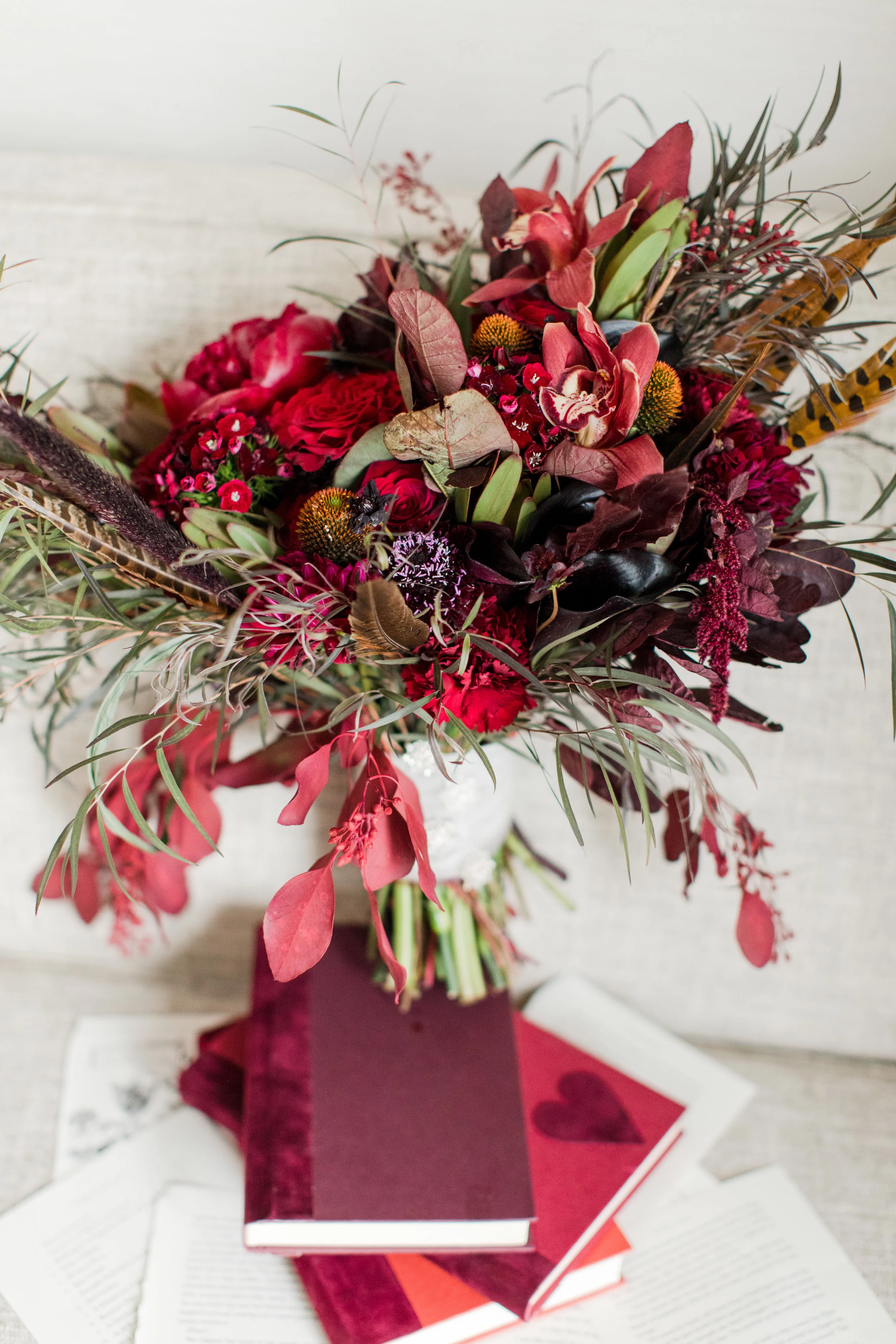 unique black and dark red bridal bouquet atop stack of books for a fall library inspired wedding photographed by jaye kogut