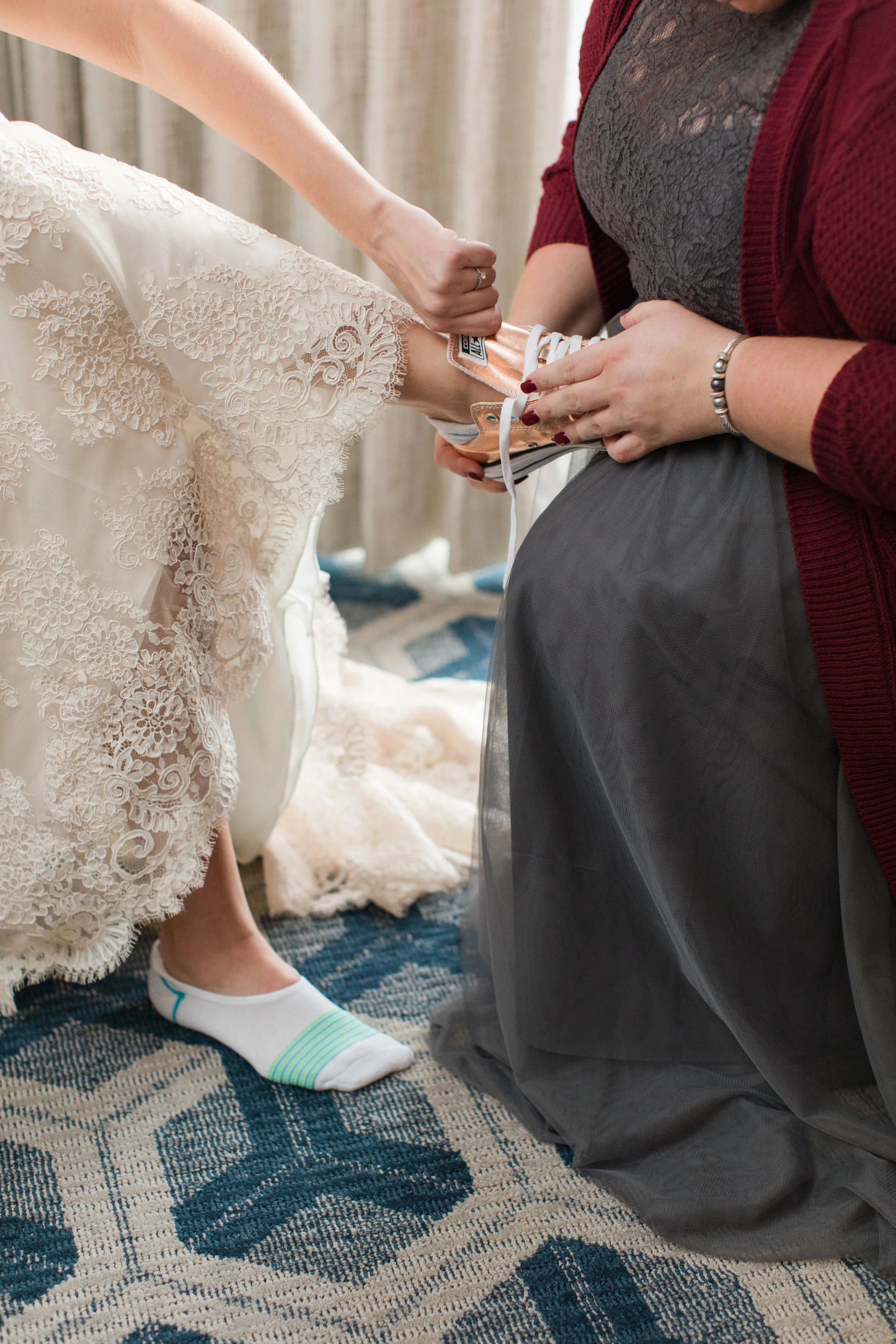 maid of honor putting rose gold converse bridal shoes on bride photographed by jaye kogut