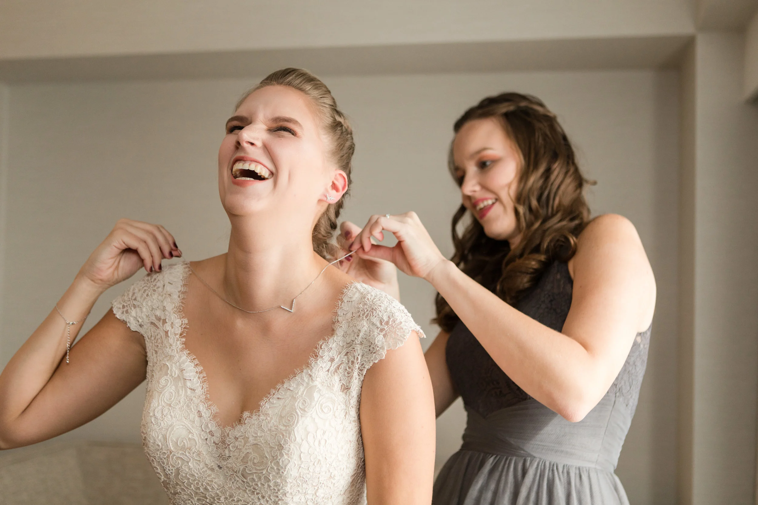 sister helps bride in lace allure bridals gown with necklace while getting ready photographed by jaye kogut