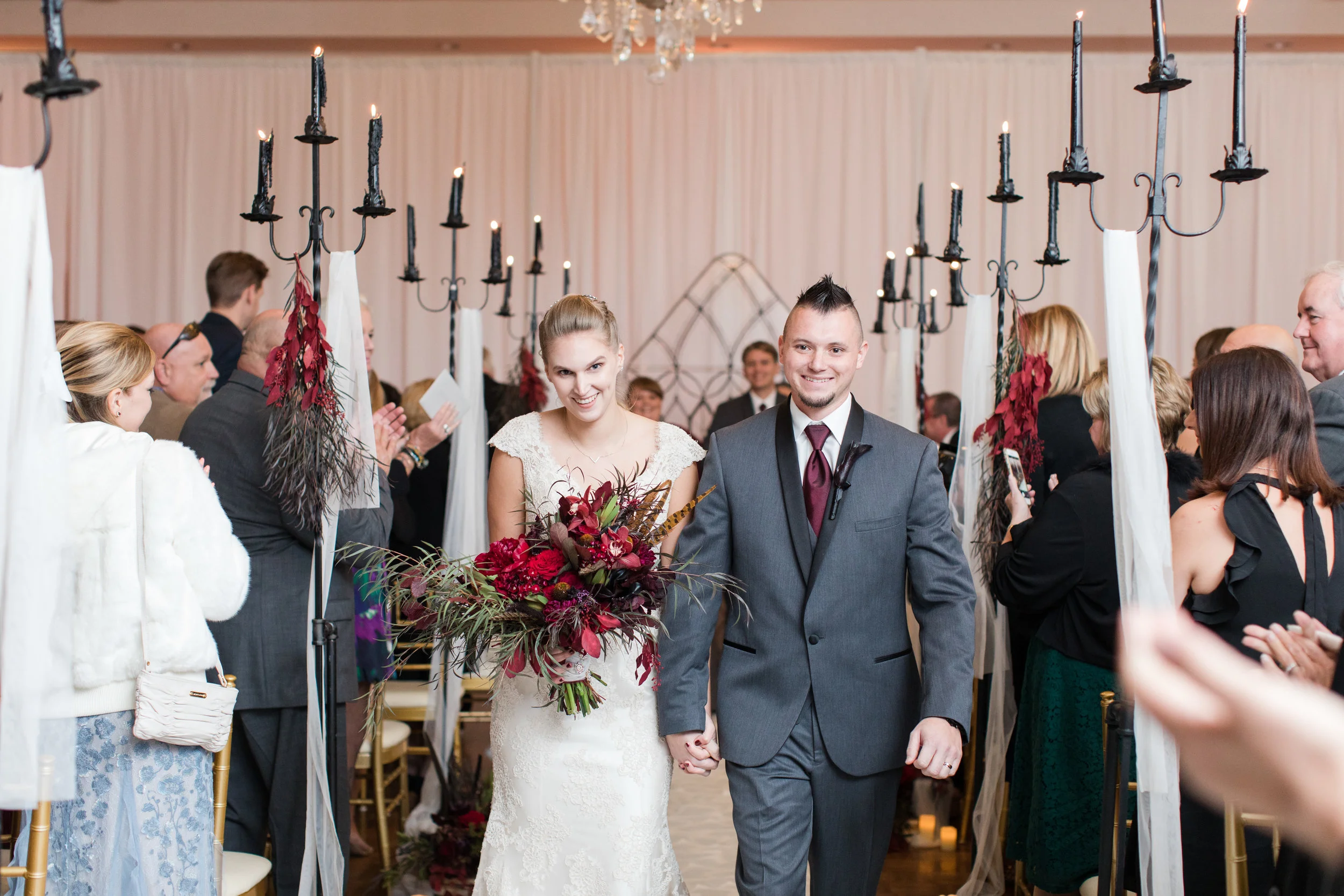 Bride and groom exit the beauty and the beast inspired ceremony at a fall library inspired wedding at Buona Sera Palazzo dark red and black fall bridal bouquet