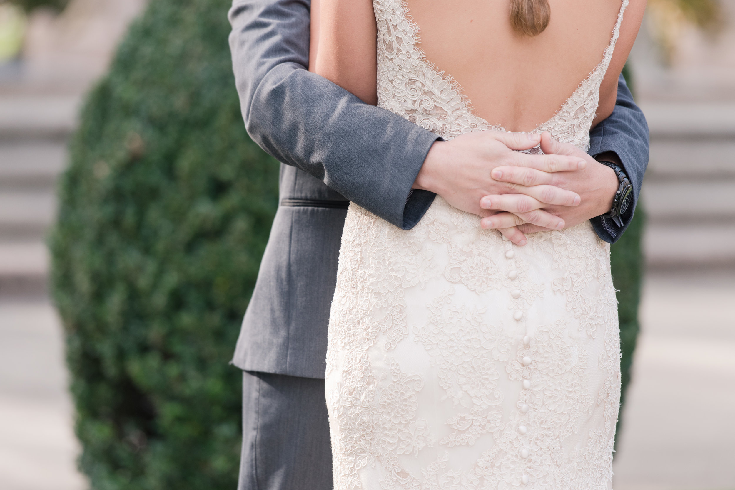 groom hugs bride in lace allure bridal wedding dress with low back and buttons