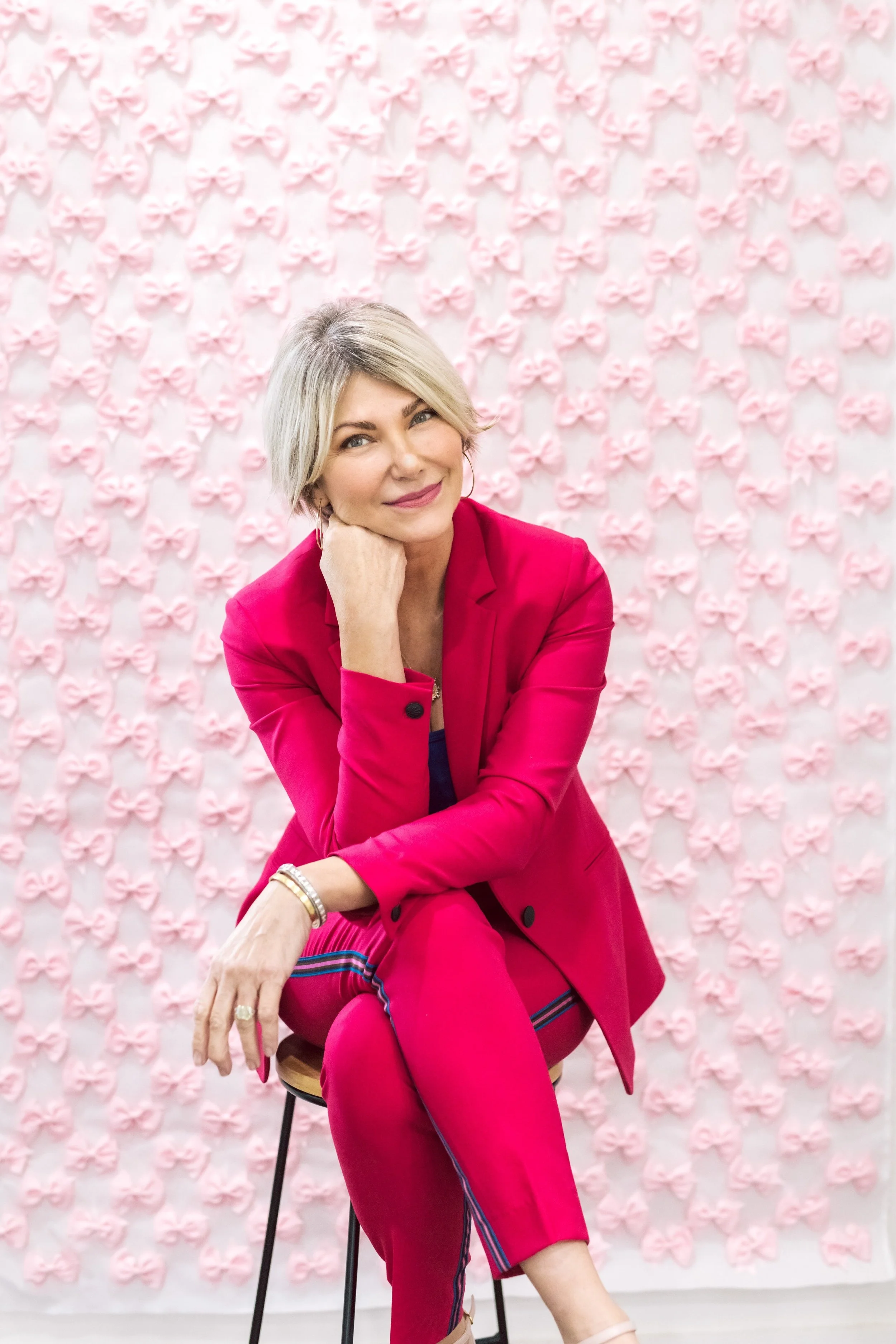Karen Hawkins, The Pink Bow Project, wearing a pink suit in front of pink bow wall