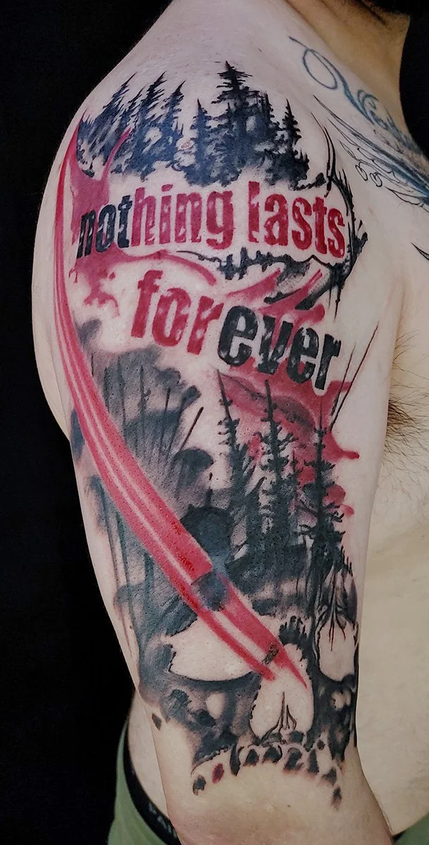 A trash polka tattoo that states "nothing lasts forever" featuring a forest and skulls.  It has a large red paint brush streak sweeping across the man's arm.  Created at a tattoo shop in Spokane, Washington.