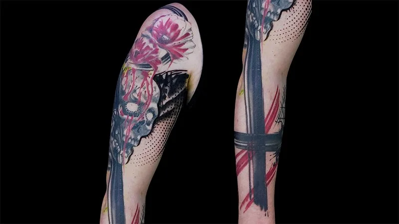 A black and red skull tattoo with trash polka design elements such as brush strokes, red streaks, and red flowers.  It has blackot work and floral patterns, done by Zack Woods of Spokane, Washington.