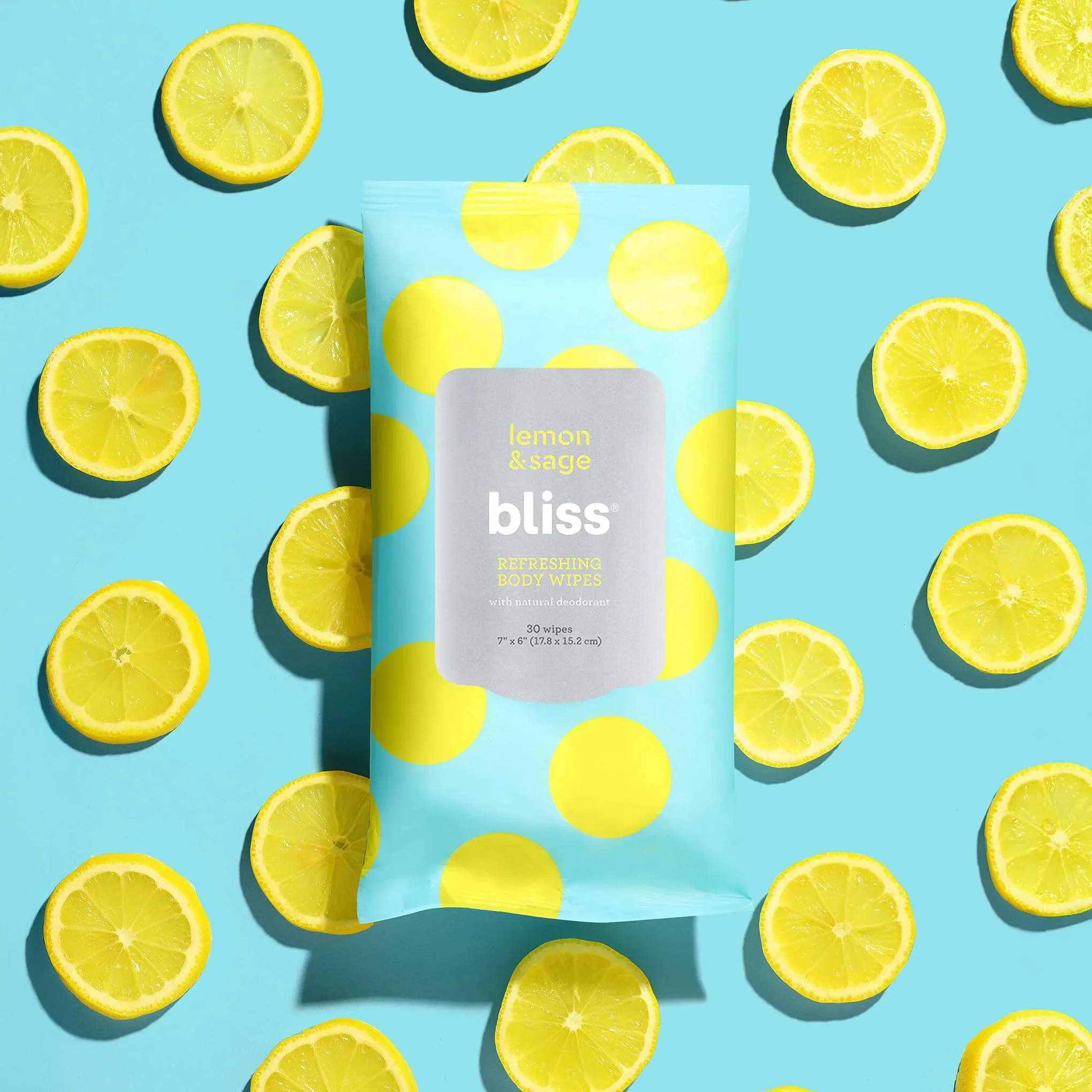 A box of bliss lemon and sage body wipes surrounded by halved bright yellow lemons on a blue background.