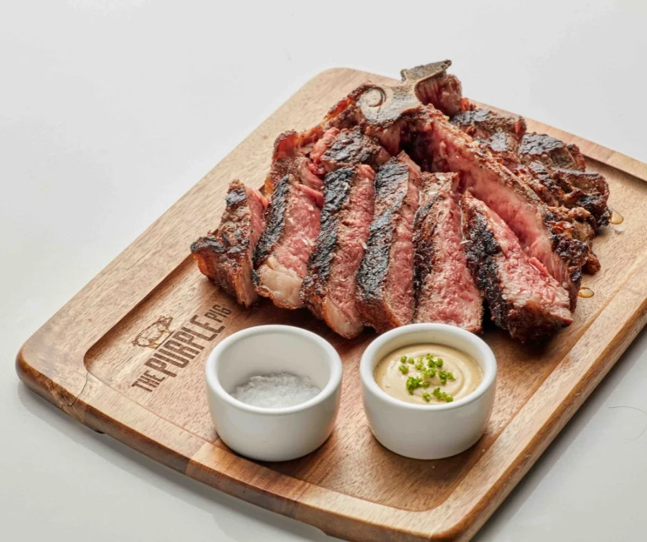 Sliced meat on a wooden cutting board with salt and condiments.