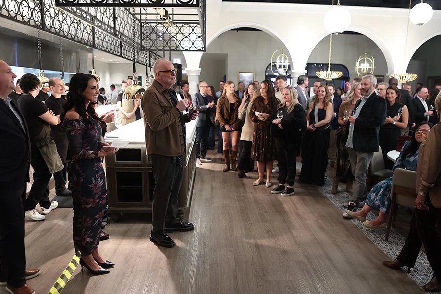 People gathered for the opening reception of The Purple Pig Oak Brook. Guests are holding drinks, listening to a speaker at a bar area inside the decorated venue.