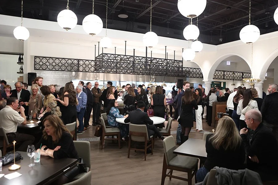 People socializing at the opening reception of The Purple Pig Oak Brook. The decor includes hanging round lights, repetitive pattern elements made of iron, and arches.
