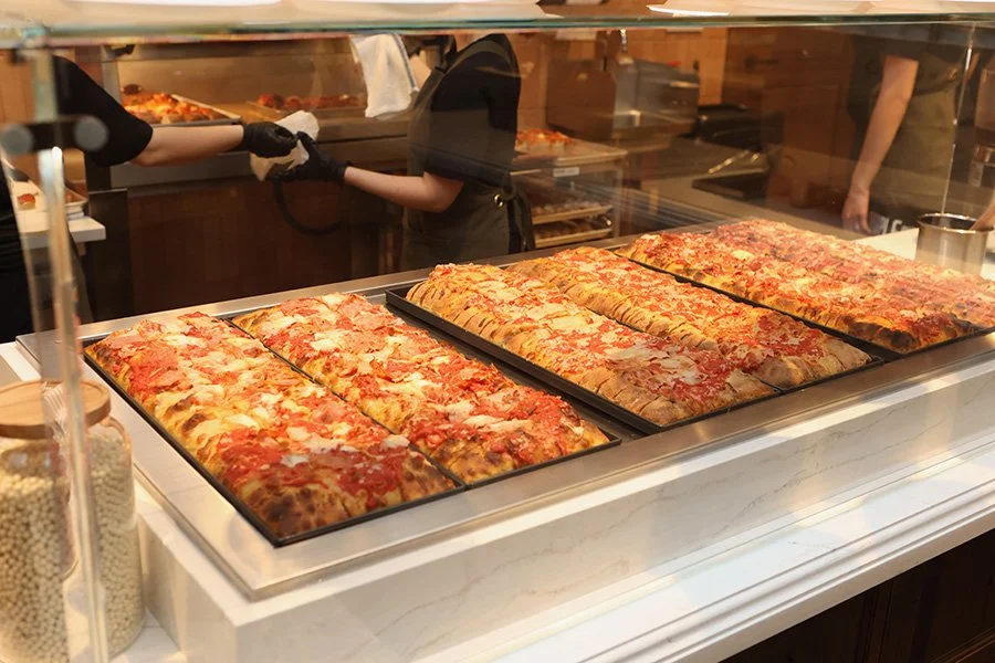 Slices of pizza displayed in a glass case at The Purple Pig opening reception.