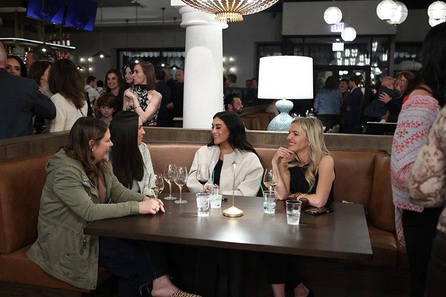 Group of four women sitting at a booth within The Purple Pig Oak Brook. They are engaged in conversation while also enjoying drinks.