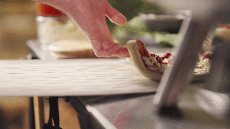 A person slicing pizza with a pizza cutter on a pizza peel.