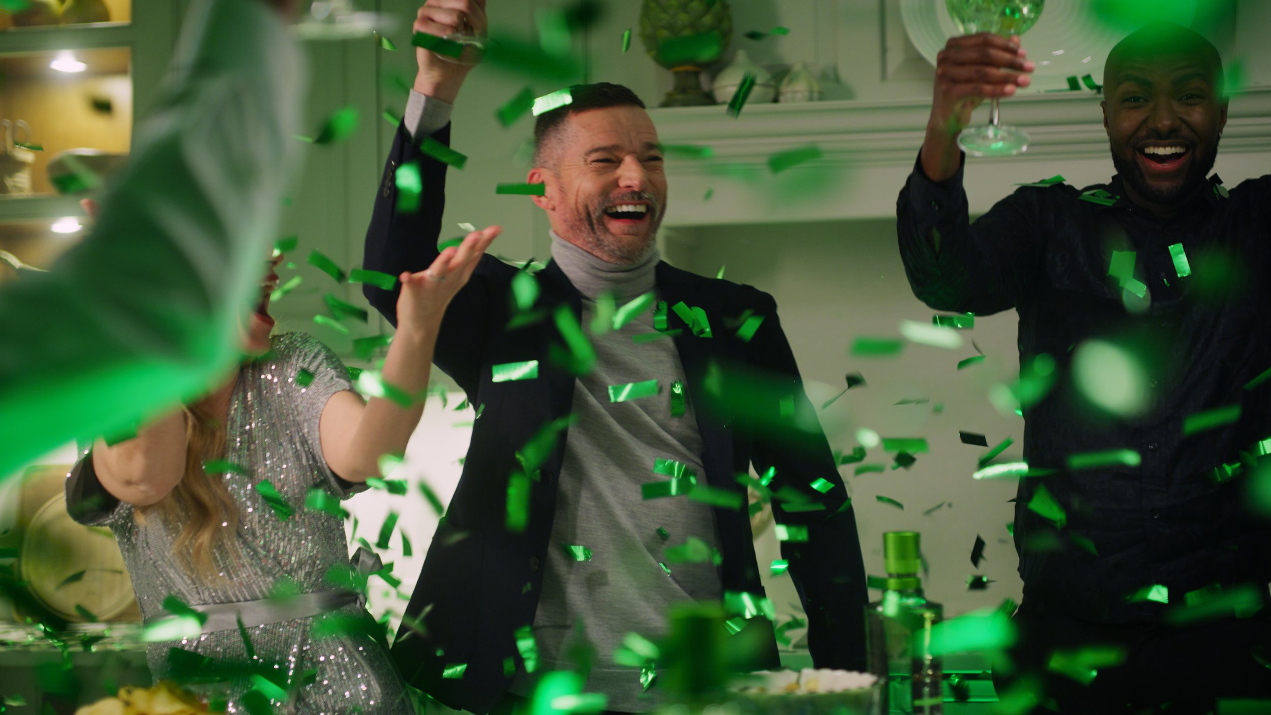 People celebrating with green confetti at a party, smiling and enjoying the moment.