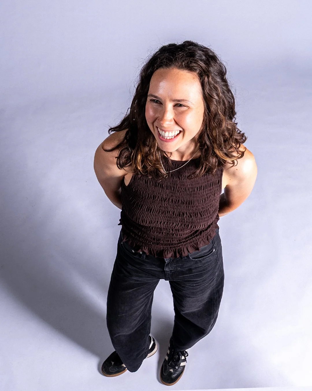 Black and white portrait of smiling woman with dark, wavy hair wearing a light-colored, ribbed button-up top, standing against a neutral background.