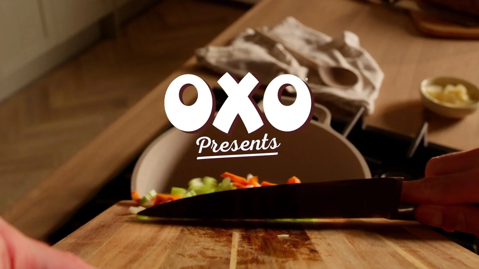 Oxo presents logo over a wooden kitchen counter with a bowl of chopped vegetables and a bowl of butter or cheese in the background.