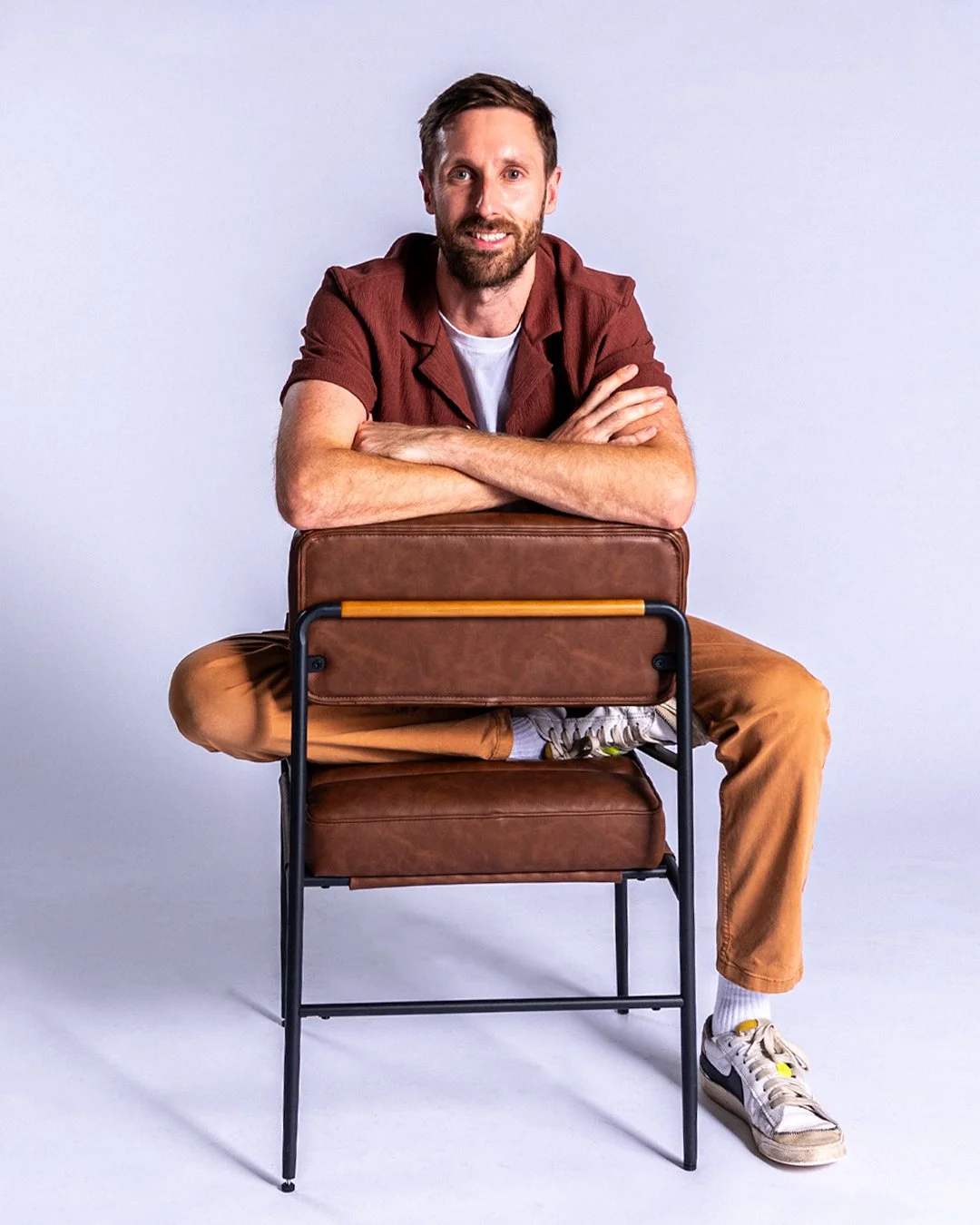 A smiling man with a beard in a white t-shirt standing against a plain background.