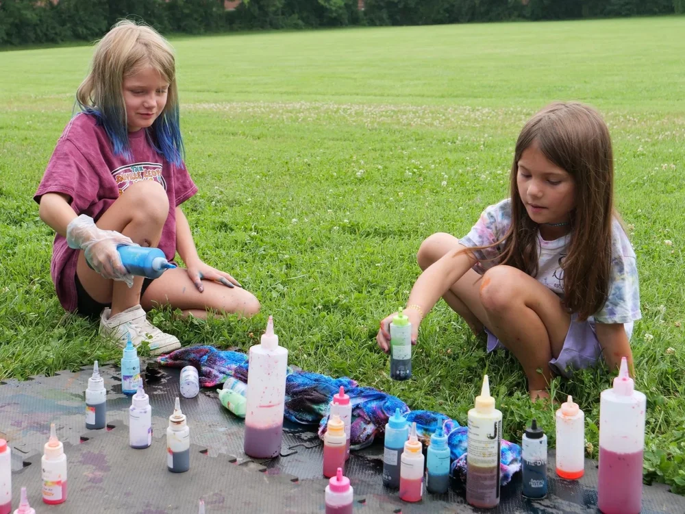 Two campers creating colorful tie-dye projects outdoors