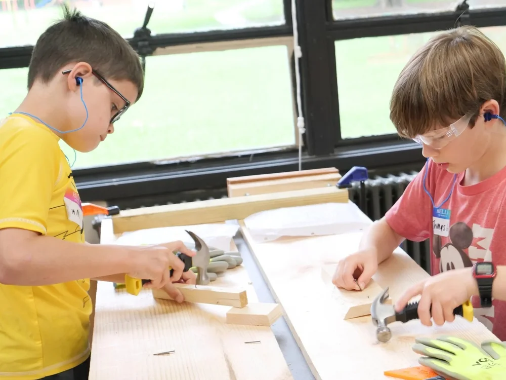 Two campers learning woodworking with hammers and safety glasses