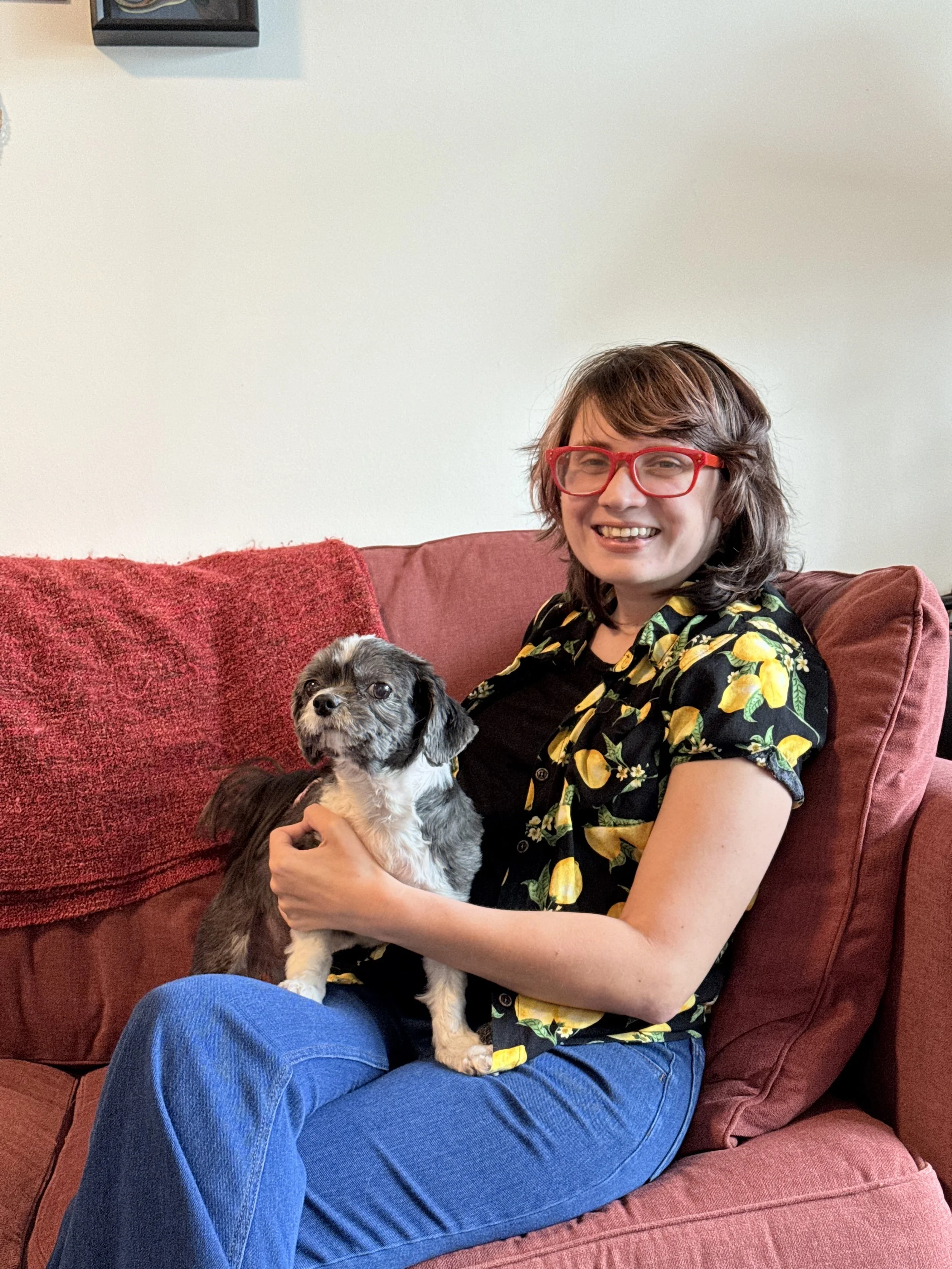 image of white person with brown hair and a small dog on a red couch