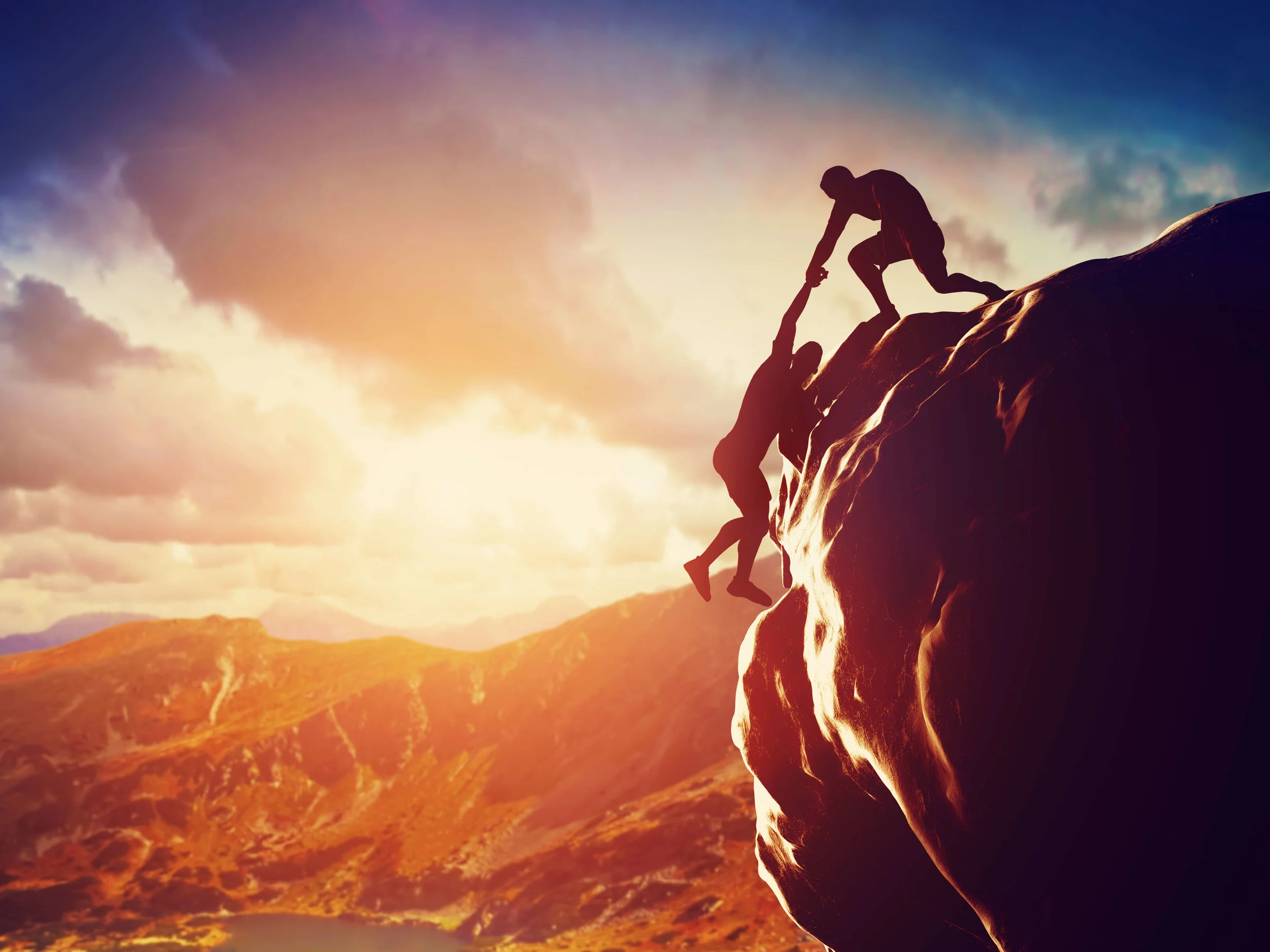 One mountain climber helping the other reach the top