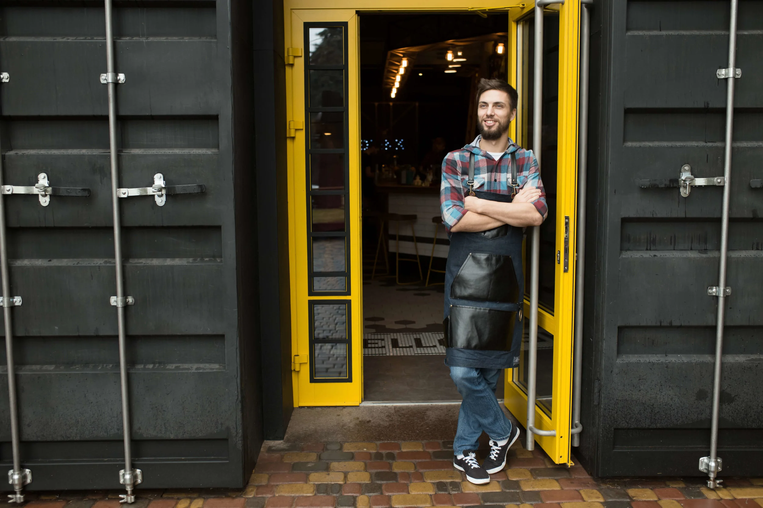 Man in apron in front of restaurant built from shipping containers