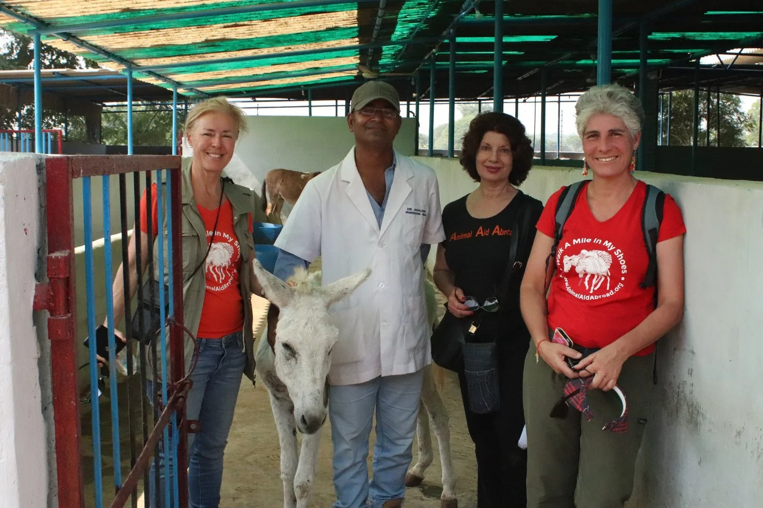 AAA Founder and members at an animal sanctuary. The women are wearing red t-shirts with the AAA logo, and the man is wearing a white veterinarian coat. The women are smiling and enjoying their visit.