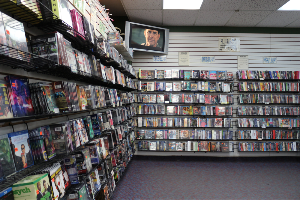  Multi levelled shelves filled with DVD cases line the corner walls with a TV in the top corner of the room. 