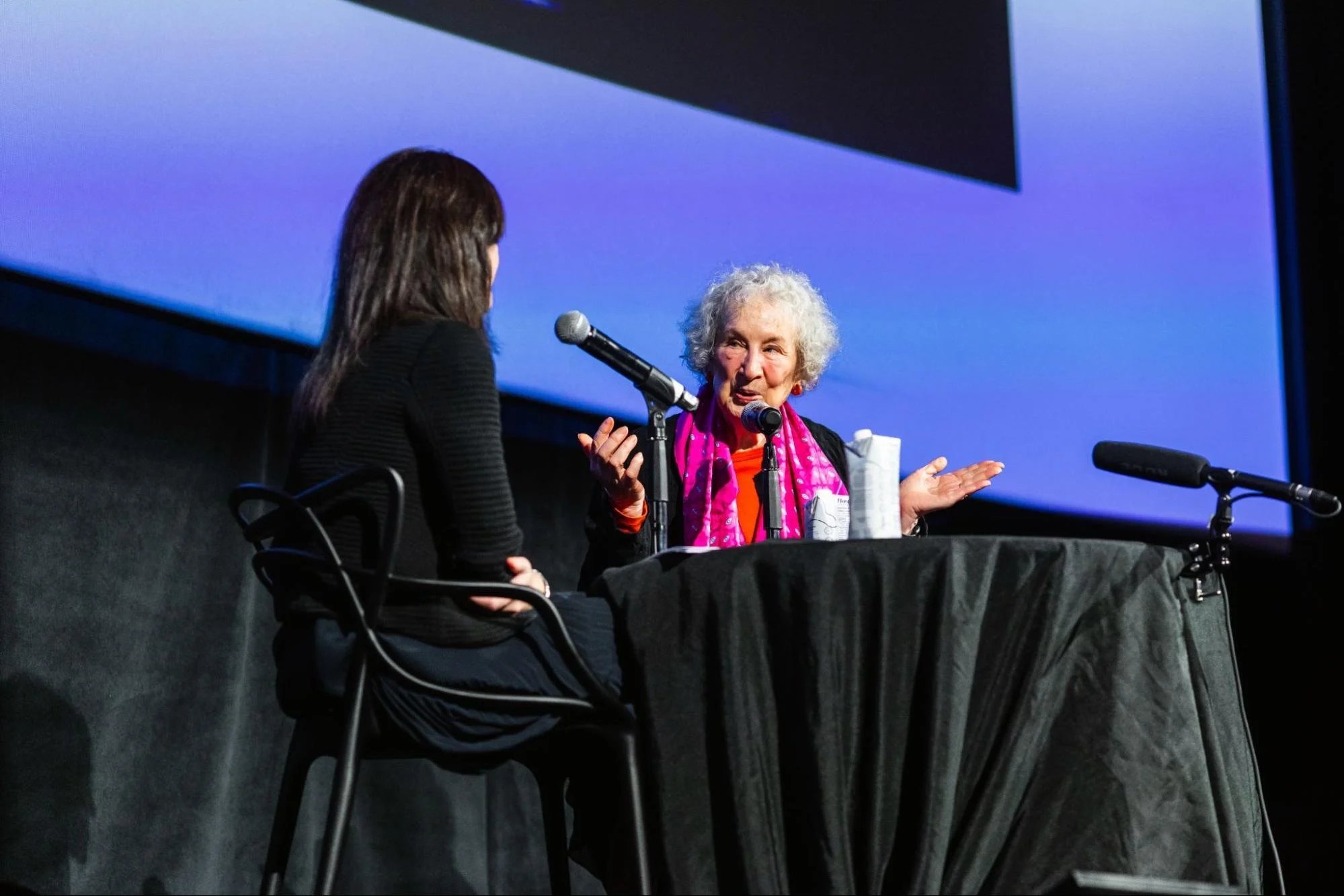 Deborah Treisman and Margaret Atwood sit at table on the Hot Docs Cinema stage
