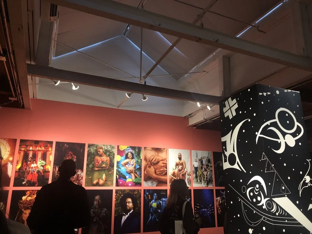 Colourful photos of people on a pink wall with a rectangular sculpture on the right