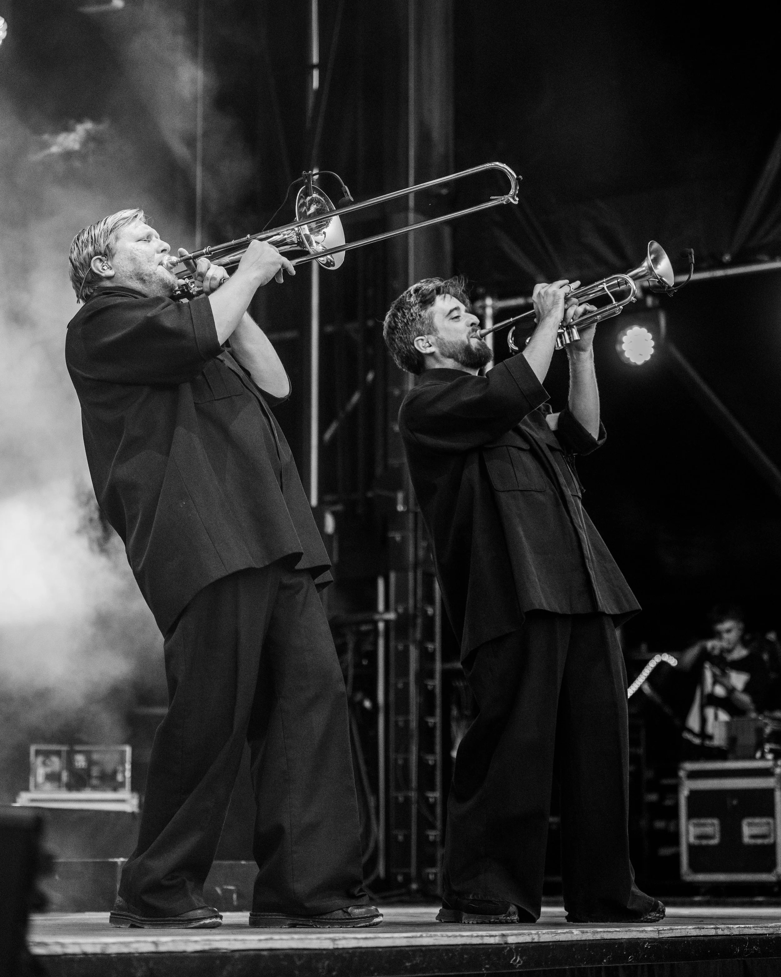 Deux musiciens jouent du trombone sur scène lors d'un concert, en noir et blanc.