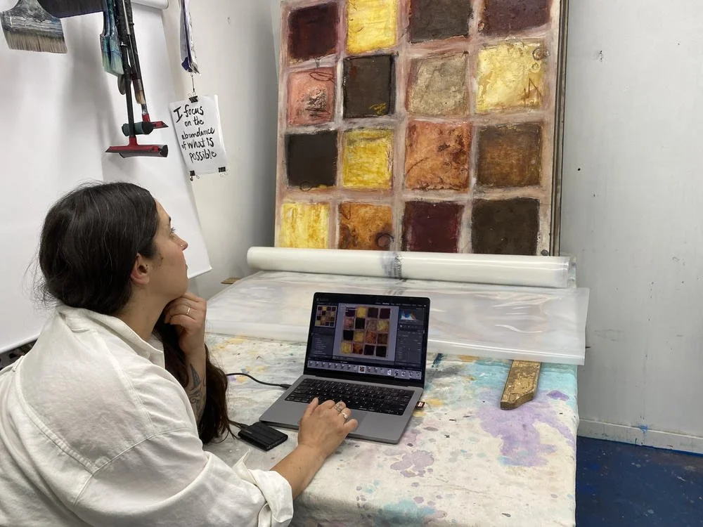 tephanie Artuso reviewing photographs on a laptop beside the painting she just documented.