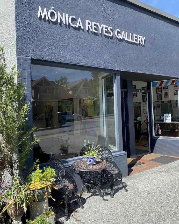 Exterior of Mónica Reyes Gallery in Vancouver's Dunbar neighbourhood, with black wrought iron bistro furniture and planters out front.